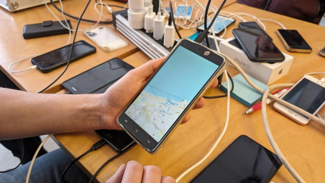 Flera smartphones anslutna till laddningskablar på ett träbord, en visar en kartapp.
